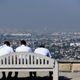Three people sit on a bench overlooking a southern California port area with a dense smog covering the skyline.